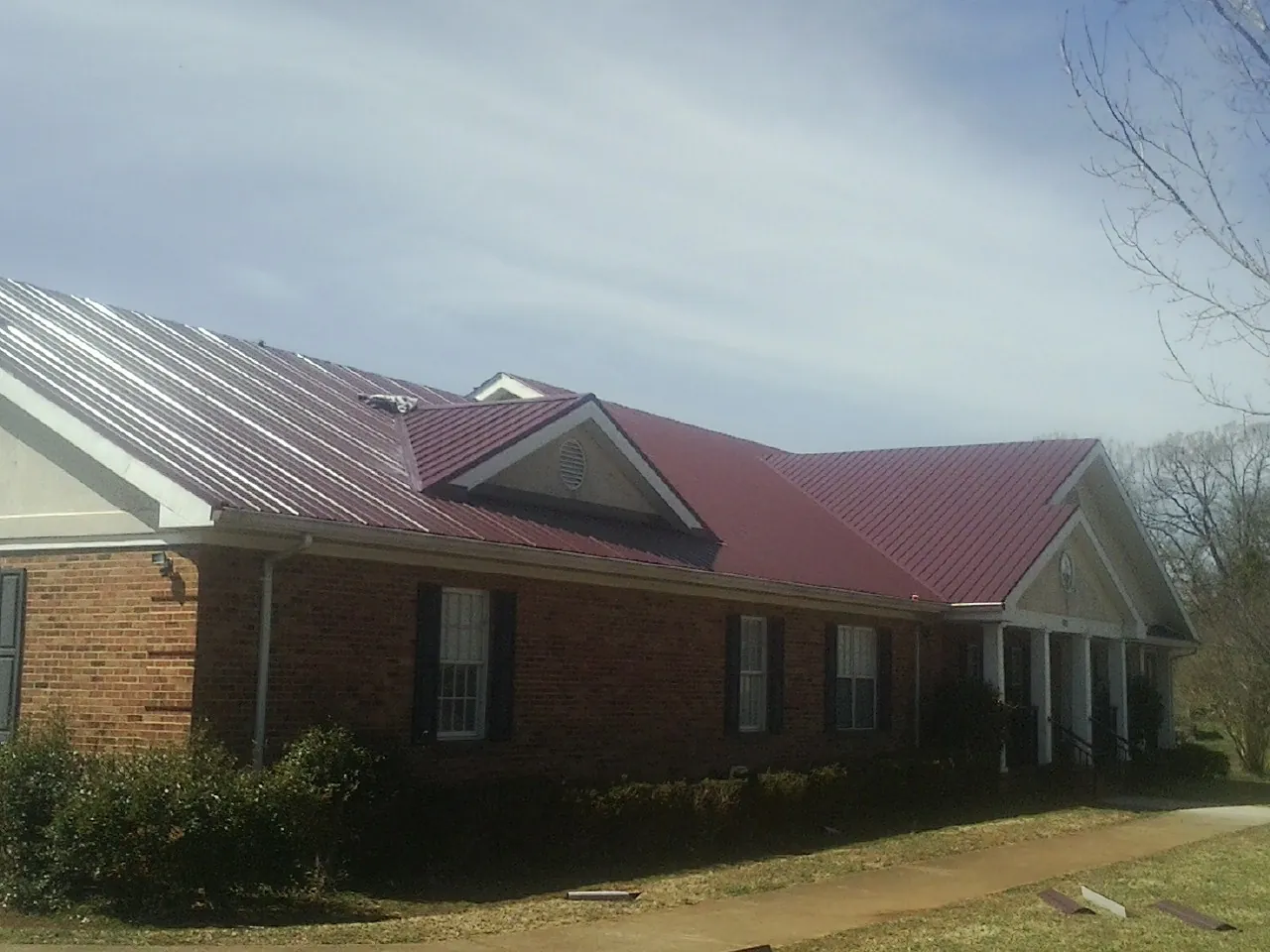 Red metal roof with gabled entries on a long brick building, from a Hail Damage Roof Repair job in Fort Campbell