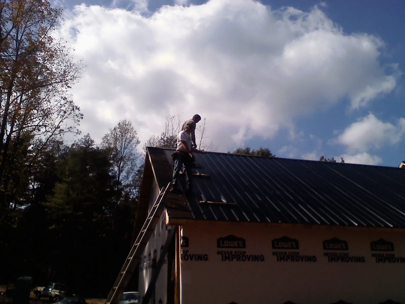 Roofer fastening dark metal panels high against a cloudy sky, from a Roof Inspection job in Fort Campbell