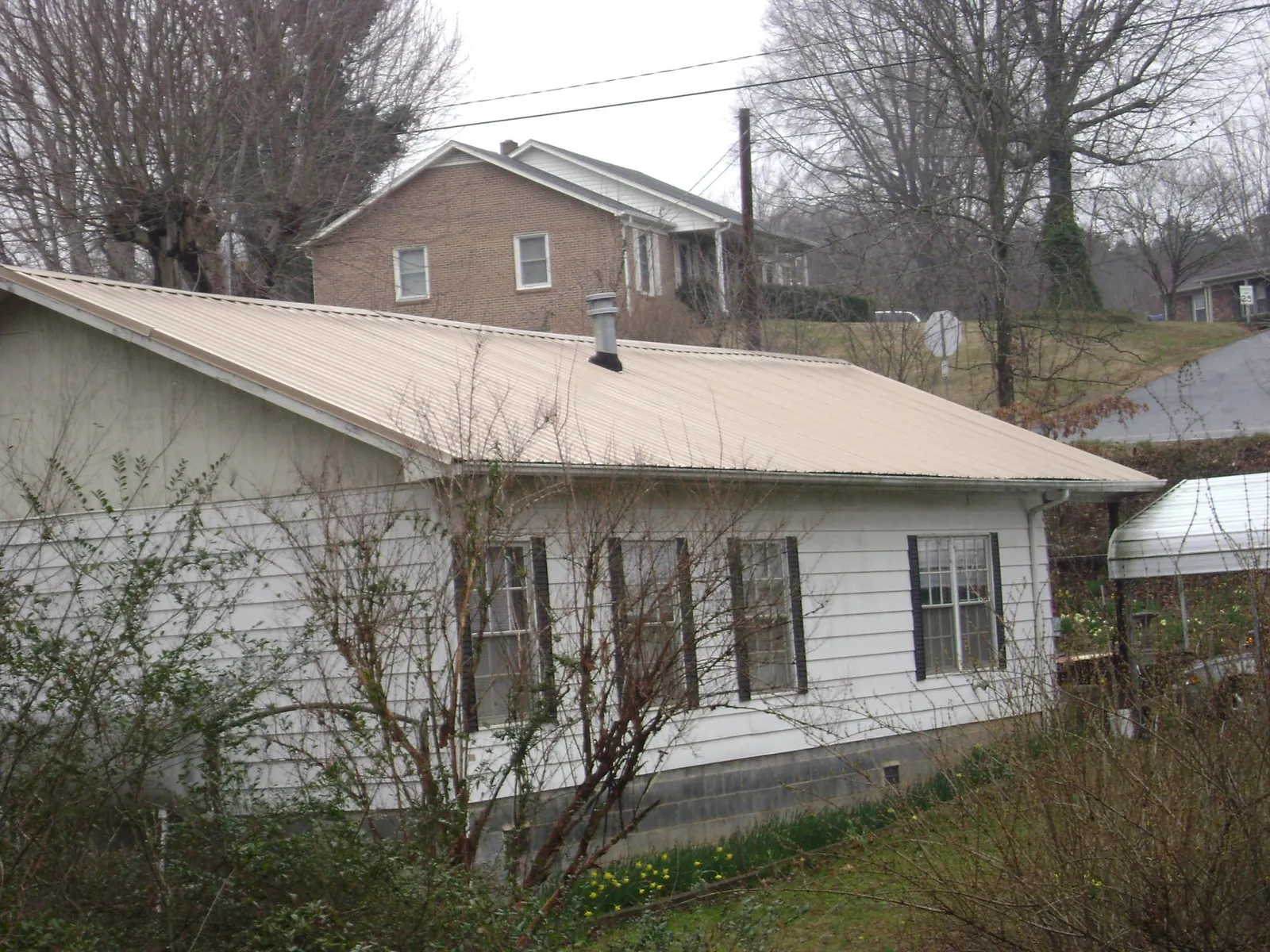 Tan metal roof on a white sided house set into a hillside — Commercial Roofing by Roofing Brothers in Fort Campbell